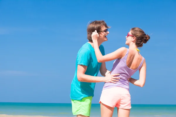 Retrato de feliz pareja joven en gafas de sol en ropa brillante coqueteando en la playa tropical —  Fotos de Stock