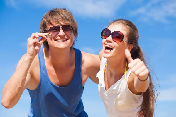 Vorderseite des glücklichen jungen Paares am Strand lächelnd und umarmt. Daumen hoch — Stockfoto