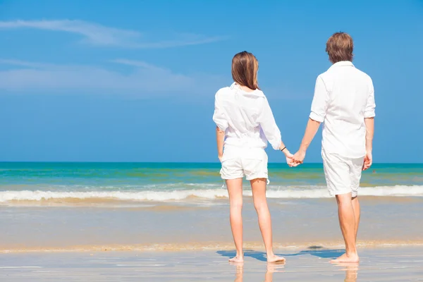 Молодая счастливая кавказская пара в белом, стоящая на пляже и смотрящая на море — стоковое фото