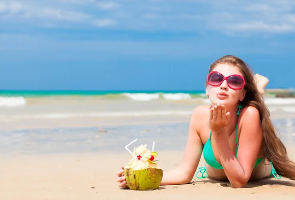 Портрет молодой женщины в бикини с кокосом на пляже, дующей воздушным поцелуем — стоковое фото