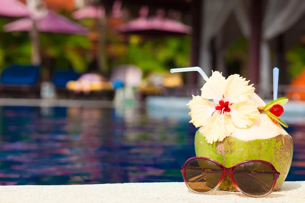 Photo de cocktail de noix de coco fraîche et lunettes de soleil roses près de la piscine de luxe — Photo