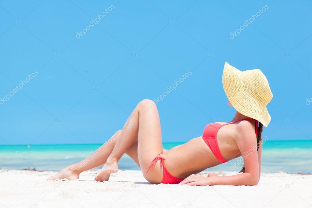 Glamorous long haired young woman in bikini, sunglasses and straw hat on tropical beach