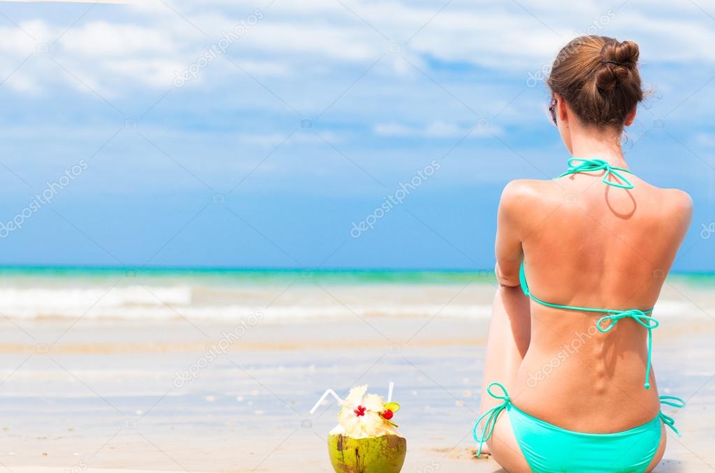 Back view of fit young woman in bikini with coconut on the beach