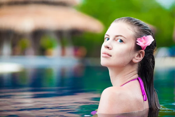 Schöne junge Frau mit Blume im Haar lächelt in Luxus-Pool — Stockfoto