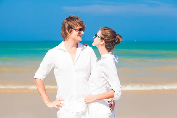 Retrato de jovem casal feliz em óculos de sol em roupas brancas flertando na praia tropical — Fotografia de Stock