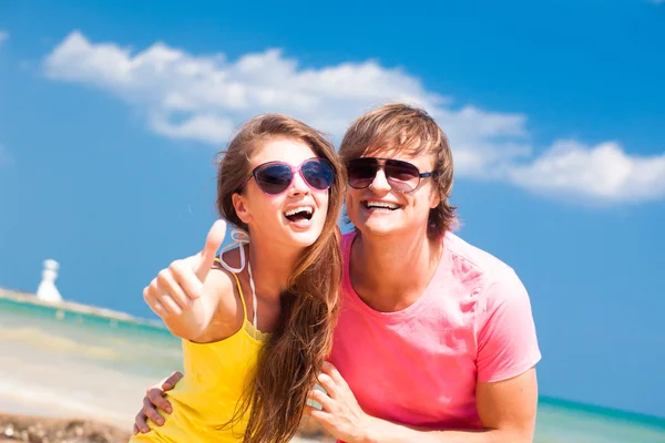 Vista frontal do jovem casal feliz na praia sorrindo e abraçando. Polegares para cima — Fotografia de Stock