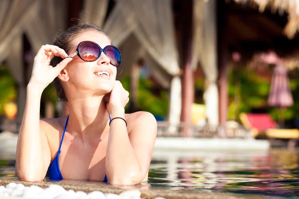 Bella giovane donna in occhiali da sole con fiore in capelli sorridente in piscina di lusso — Foto Stock