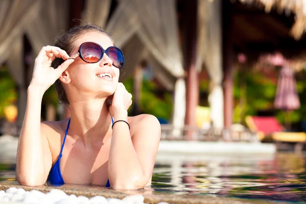 Mulher bonita em óculos de sol com flor no cabelo sorrindo na piscina de luxo — Fotografia de Stock