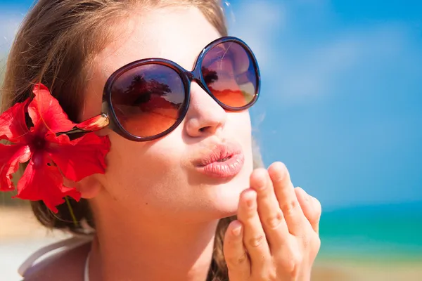 Портрет молодої жінки в сонцезахисних окулярах, що дме повітряний поцілунок на пляжі — стокове фото