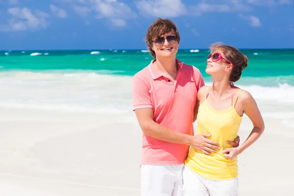 Par i ljusa kläder kramas på tropisk strand — Stockfoto