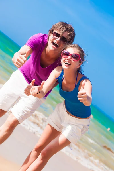 Portrait de jeune couple heureux en lunettes de soleil s'amusant sur la plage tropicale. Pouce en l'air — Photo