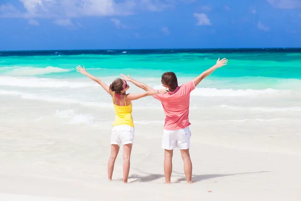 Visão traseira do casal acenando as mãos na praia tropical — Fotografia de Stock