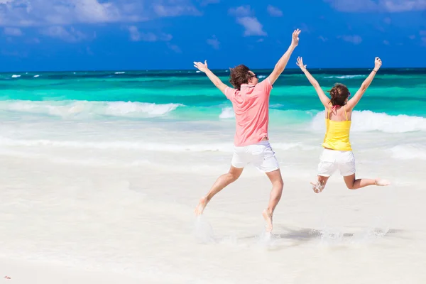 Ungt par i ljusa kläder hoppa på stranden — Stockfoto