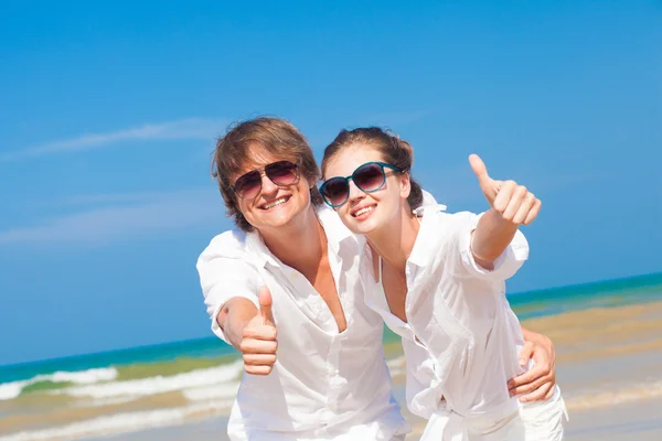 Vista frontale di felice giovane coppia sulla spiaggia sorridente e abbraccio. Pollici in alto — Foto Stock