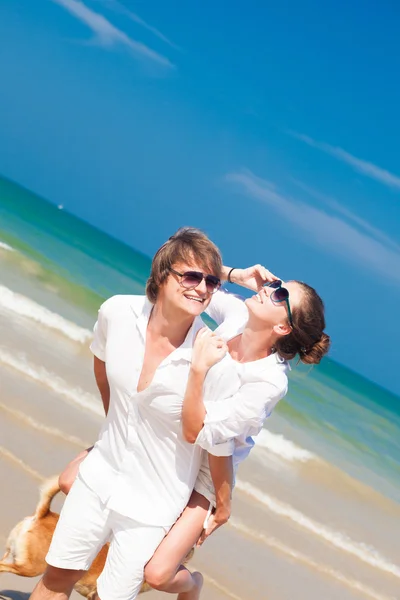 Joyeux couple sur une plage tropicale avec un chien à leurs pieds — Photo