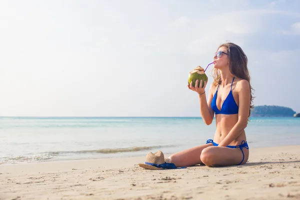 Felice giovane donna in bikini blu bere latte di cocco sulla spiaggia — Foto Stock
