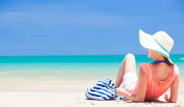 Вид ззаду жінки з смугастим мішком і солом'яним капелюхом, що лежить на пляжі — стокове фото