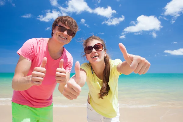 Retrato de jovem casal feliz em óculos de sol se divertindo na praia tropical. Polegares para cima — Fotografia de Stock