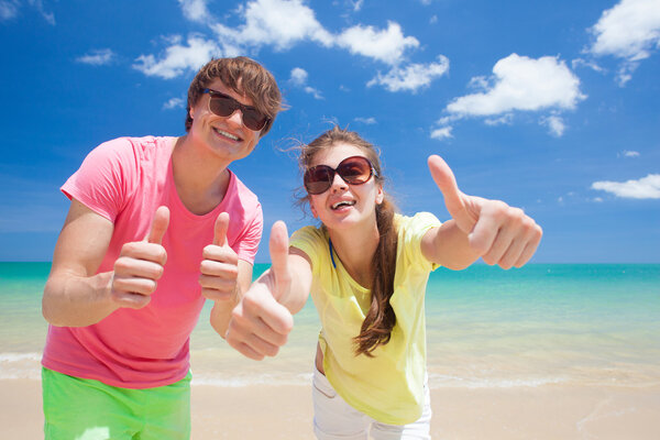 Portrait of happy young couple in sunglasses having fun on tropical beach. Thumbs up