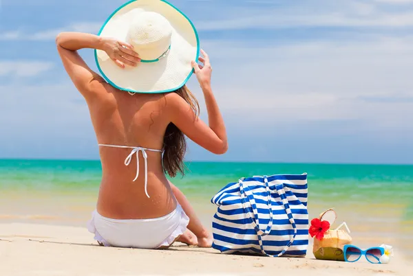 Vista trasera de una mujer en bikini y sombrero de paja con bolsa de playa y cóctel de coco —  Fotos de Stock