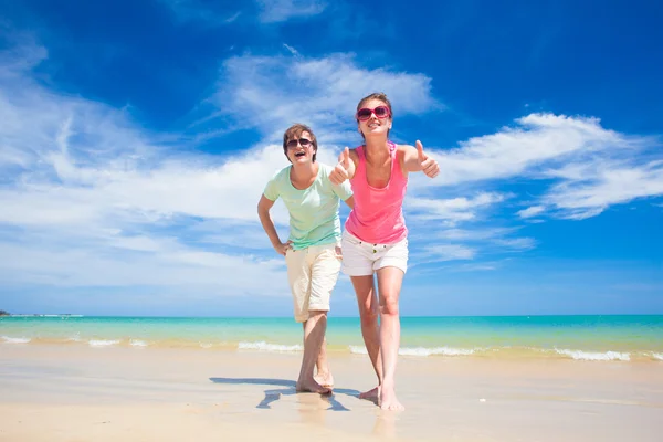 Retrato de pareja joven feliz en ropa brillante y gafas de sol divirtiéndose en la playa tropical — Foto de Stock