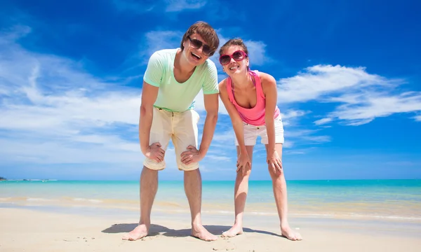 Retrato de pareja joven feliz en ropa brillante y gafas de sol divirtiéndose en la playa tropical —  Fotos de Stock