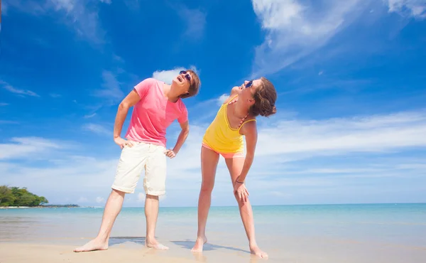 Portrait de jeune couple heureux en vêtements lumineux et lunettes de soleil s'amusant sur la plage tropicale — Photo