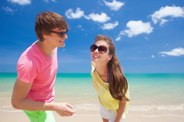 Retrato de pareja joven feliz en ropa brillante y gafas de sol divirtiéndose en la playa tropical —  Fotos de Stock