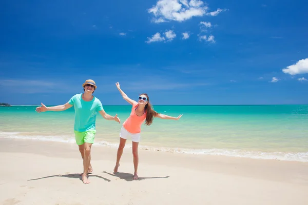 Retrato de jovem casal feliz em roupas brilhantes e óculos de sol se divertindo na praia tropical — Fotografia de Stock