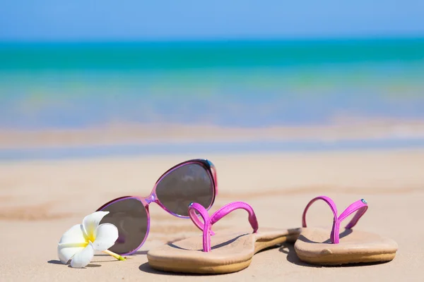 Infradito, occhiali da sole a forma di cuore e frangipani sulla spiaggia tropicale — Foto Stock