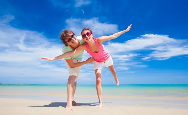 Portrait of happy young couple in bright clothes and sunglasses having fun on tropical beach — Stock Photo, Image