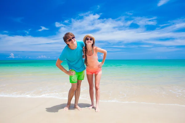 Retrato de jovem casal feliz em roupas brilhantes e óculos de sol se divertindo na praia tropical — Fotografia de Stock