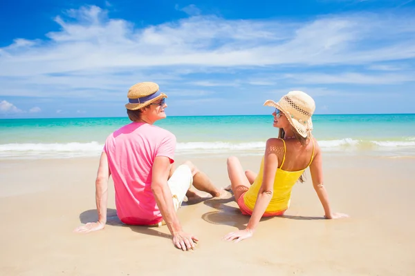 Feliz joven pareja teniendo en sombreros de paja sentado en la playa tropical — Foto de Stock