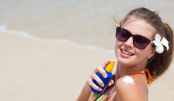 Jonge vrouw in zonnebril zetten zon crème op schouder — Stockfoto