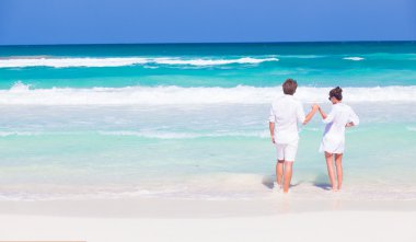 arkadan görünüşü mutlu genç bir çift beyaz giysiler ve eğleniyor tropikal plaj güneş gözlüğü