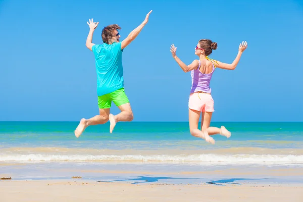 Visão traseira do jovem casal feliz em roupas brilhantes pulando na praia — Fotografia de Stock