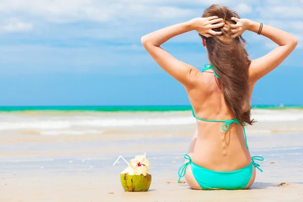 Jovem mulher com coco sentado na praia — Fotografia de Stock