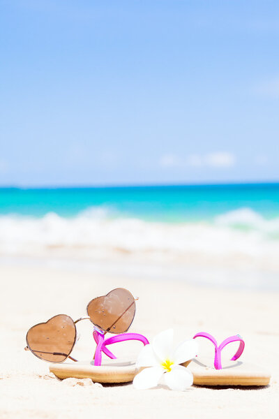 flip flops, heart-shaped sunglasses and frangipani on tropical beach