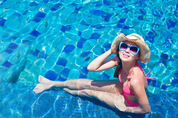 Jovem mulher de chapéu de palha e biquíni relaxante na piscina — Fotografia de Stock