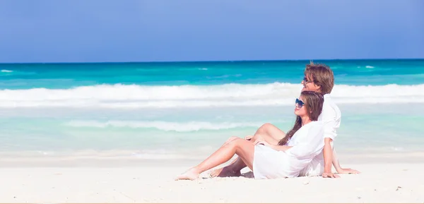 Junges Paar in weißen Kleidern sitzt am tropischen Strand — Stockfoto