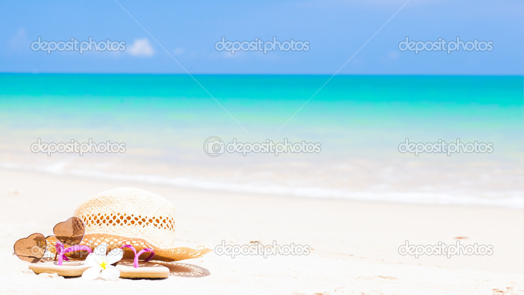 flip flops, heart-shaped sunglasses, straw hat and frangipani on tropical beach