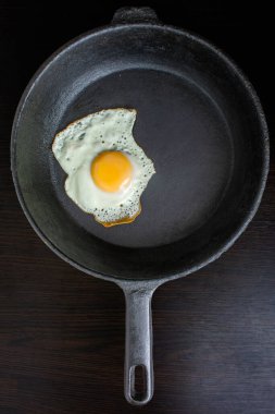 scrambled eggs with yellow yolk in a cast iron pan. Isolated on dark painted wood from above.