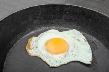 scrambled eggs with yellow yolk in a cast iron pan. Isolated on dark painted wood from above.