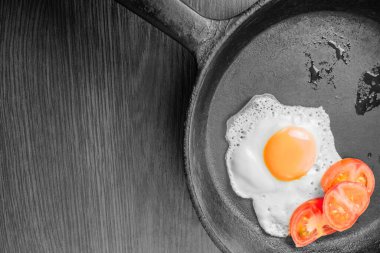 Egg, sunny side up, with fresh tomatoes in a black pan