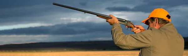 一个拿着枪的猎鸭人在落日的映衬下穿过草地 — 图库照片