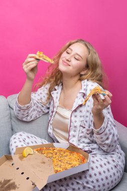 Kız kanepede oturur ve pizza yer..