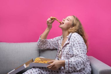 Kız kanepede oturur ve pizza yer..