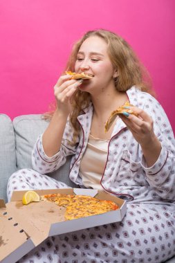 Kız kanepede oturur ve pizza yer..