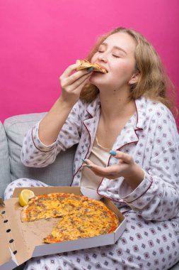Kız kanepede oturur ve pizza yer..
