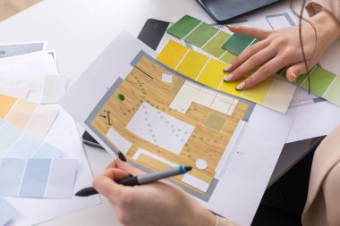 Masada oturan genç bir tasarımcı kız tablete resim çizer. Bilgisayarda iş hesaplamaları yapar.